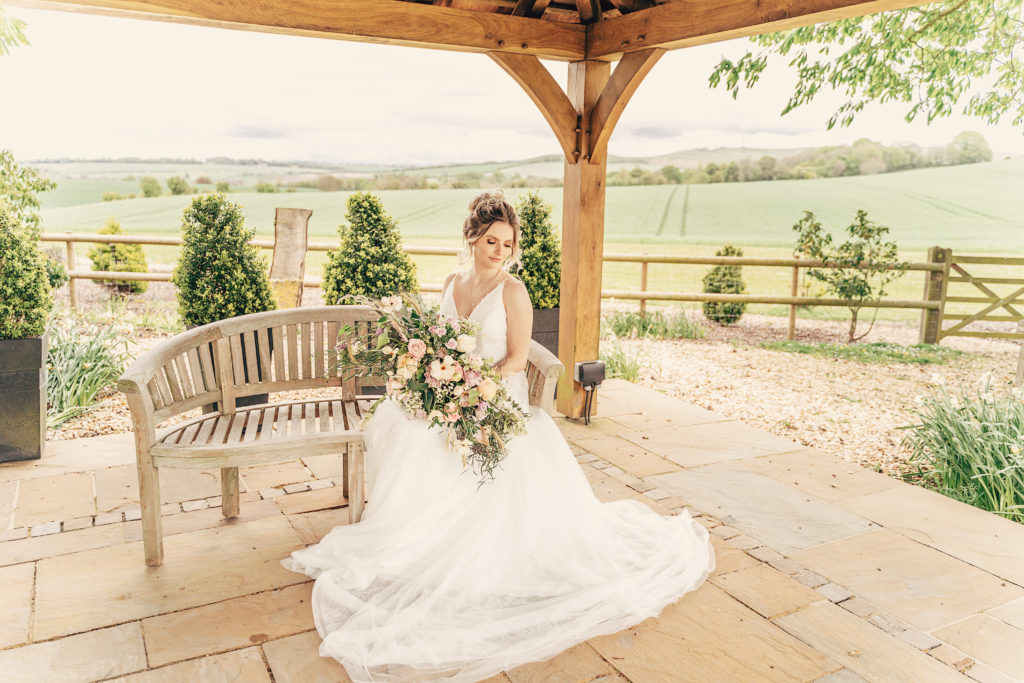 Bride sat on bench with flowers at Wellington Barn, Wedding