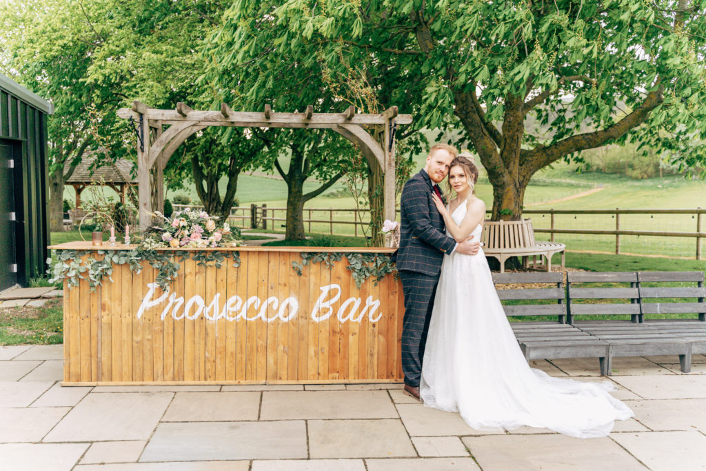 Bride and groom stood in front of prosecco Bar at Wellington Barn Wedding