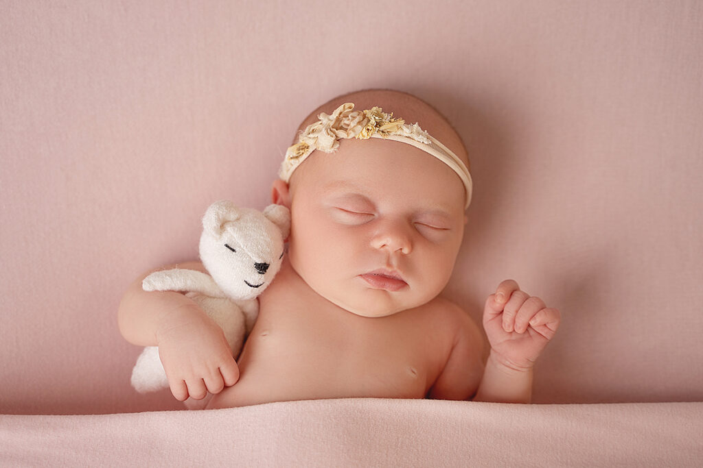 newborn baby girl on pink blanket holding a white teddy bear