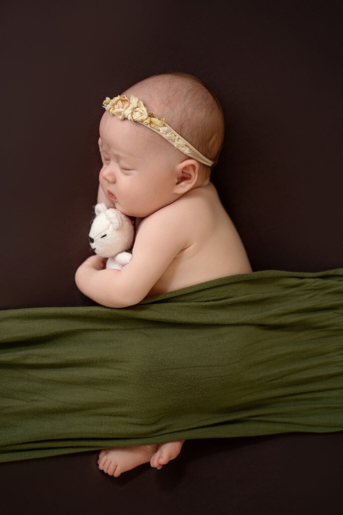 newborn baby on brown backdrop, with green blanket over them 
